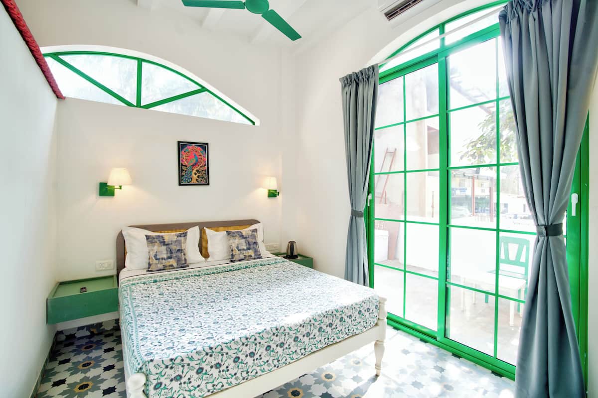 A bedroom with a bed, a window with curtains, a wall-mounted lamp, and a picture.