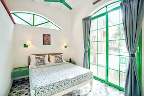 A bedroom with a bed, a window with curtains, a wall-mounted lamp, and a picture. - Casa Arvona (Calangute)