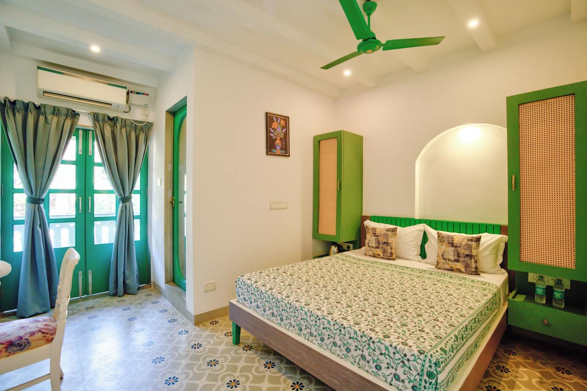 A bedroom with a bed, green walls, a ceiling fan, and a window with curtains.