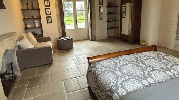 A bedroom with a bed, a sofa, a wooden wardrobe, a window with a view, and a tiled floor.