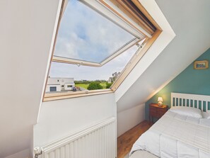 A bedroom with a skylight, a bed, a nightstand, and a view of a house and greenery. - House for 6 with jacuzzi and large garden (Treffiagat)