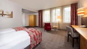 Et hotelværelse med seng, skrivebord, stol, skab og lampe.