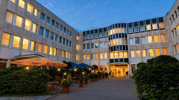 En hotelgård med udendørs siddepladser, plantekasser og en godt oplyst indgang.
