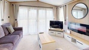 Un salon moderne avec un canapé, un téléviseur et une grande fenêtre agrémentée de rideaux.