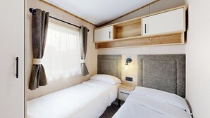 Ein gemütliches Schlafzimmer mit zwei Betten, einem Fenster mit Vorhängen, einem Nachttisch mit Lampe und integrierten Schränken.