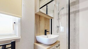 Ein modernes Badezimmer mit einem weißen Waschtisch, einem Holzschrank und einer Duschkabine aus Glas.