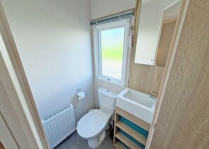 Ein kleines Badezimmer mit Toilette, Fenster, Heizkörper und Waschbecken.