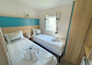 Habitación de hotel con dos camas, una ventana con cortinas, una planta pequeña en la pared y un cabecero de madera.
