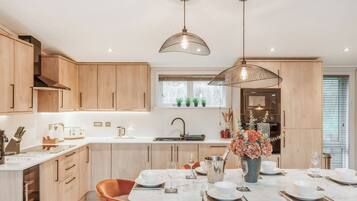 A modern kitchen with wooden cabinets, a central island with seating, pendant lighting, and a view of the outdoors.