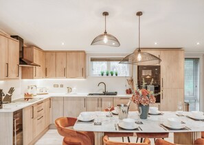 A modern kitchen with wooden cabinets, a central island with seating, pendant lighting, and a view of the outdoors.