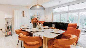 A modern dining area with a marble table, orange chairs, and a black sofa.