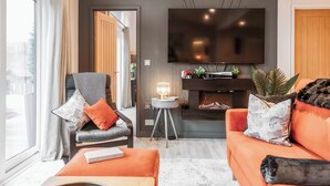 Ein modernes Wohnzimmer mit Sofa, Sesseln und einem flachbildfernseher an der Wand.