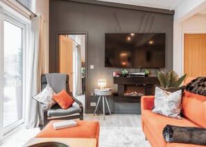A modern living room with a sofa, armchair, and a flat-screen TV mounted on the wall.