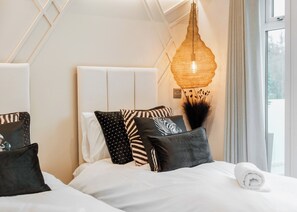 A modern hotel room with a large bed, a unique woven light fixture, and a view of the outdoors.