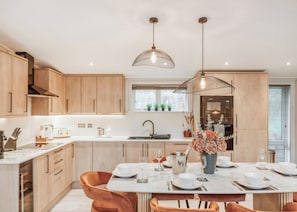 Una cocina moderna con armarios de madera, una isla central con asientos, iluminación colgante y vistas al exterior.
