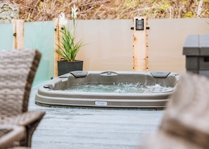 Un jacuzzi con una terraza de madera, una planta en maceta y una valla de madera al fondo.