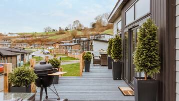 A deck with a grill, potted plants, and a view of a residential area.