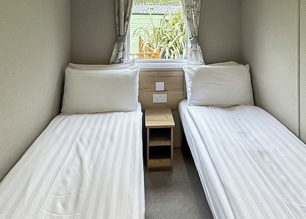 A small, single-room accommodation with two single beds, a wooden nightstand, and a window with curtains.