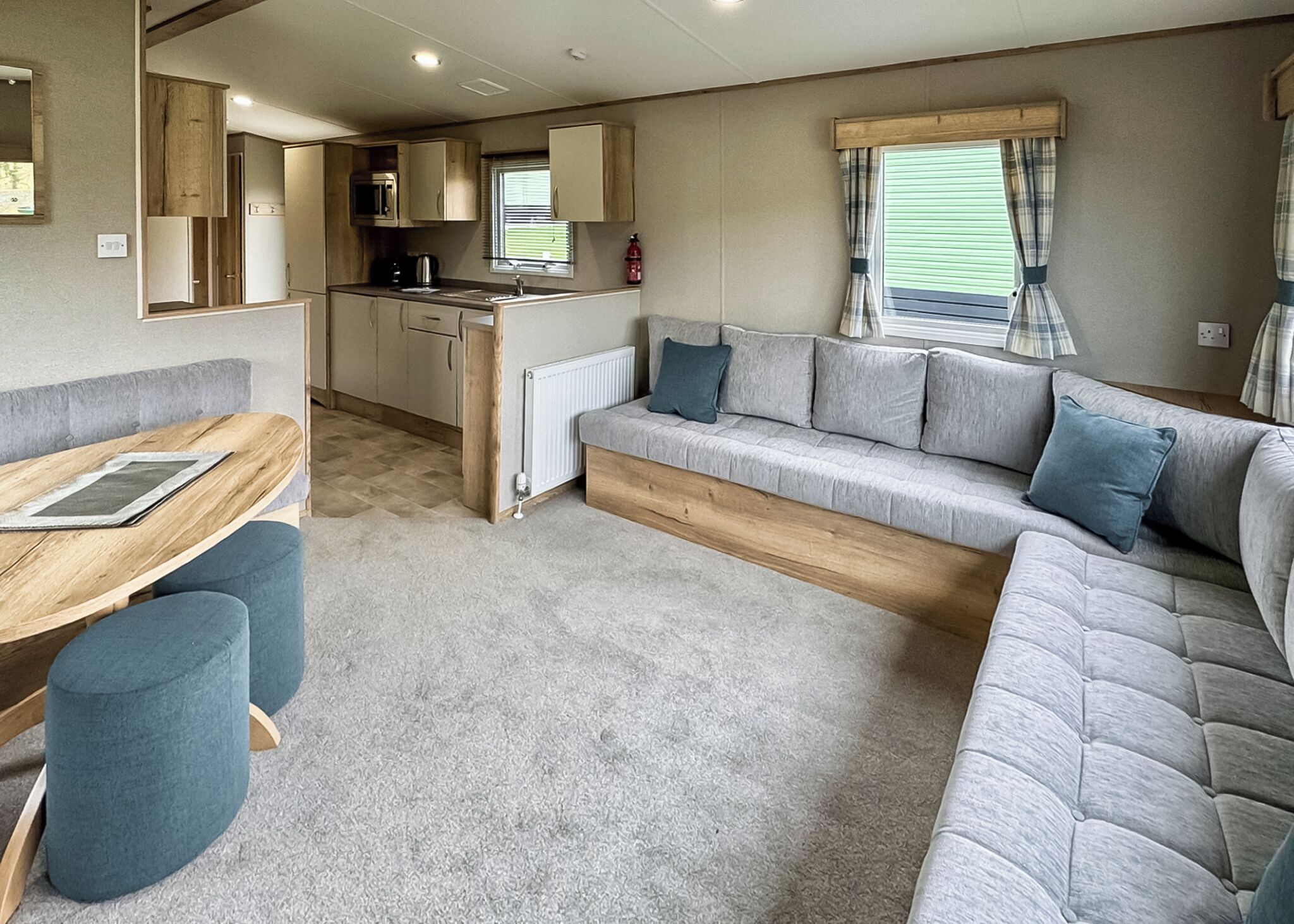 A caravan interior with a kitchenette, a sofa, a dining table, and a window with curtains.