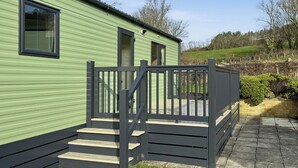 A green mobile home with a wooden deck and a staircase leading to a door. - Luxury caravan with one double and one twin room. (Llanrhystud, Cardiganshire)
