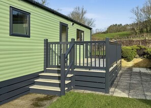 A green mobile home with a wooden deck and a staircase leading to a door. - Luxury caravan with one double and one twin room. (Llanrhystud, Cardiganshire)