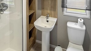 A bathroom with a pedestal sink, toilet, and a small trash bin. - Luxury caravan with one double and one twin room. (Llanrhystud, Cardiganshire)