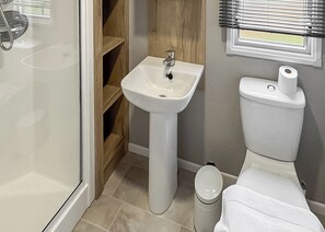 A bathroom with a pedestal sink, toilet, and a small trash bin. - Luxury caravan with one double and one twin room. (Llanrhystud, Cardiganshire)