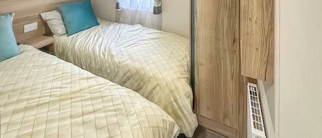 Ein Schlafzimmer mit zwei Betten, einem fensterbelaubten Fenster und einer Heizung.
