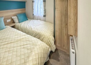 Ein Schlafzimmer mit zwei Betten, einem fensterbelaubten Fenster und einer Heizung.
