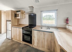 Eine moderne Küche mit Holzschränken, einem eingebauten Ofen, einem Herd, einer Mikrowelle und einem Fenster mit Jalousien.