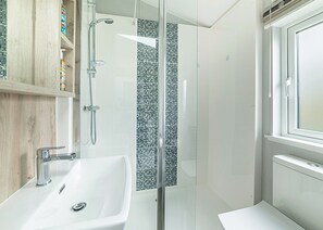 Une salle de bain moderne avec une douche à parois de verre, un lavabo blanc et une fenêtre.