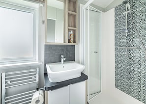 Un baño con un lavamanos blanco, una cabina de ducha de vidrio y una pared de ducha con azulejos.