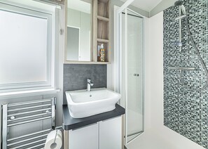 A bathroom with a white sink, a glass shower enclosure, and a tiled shower wall.