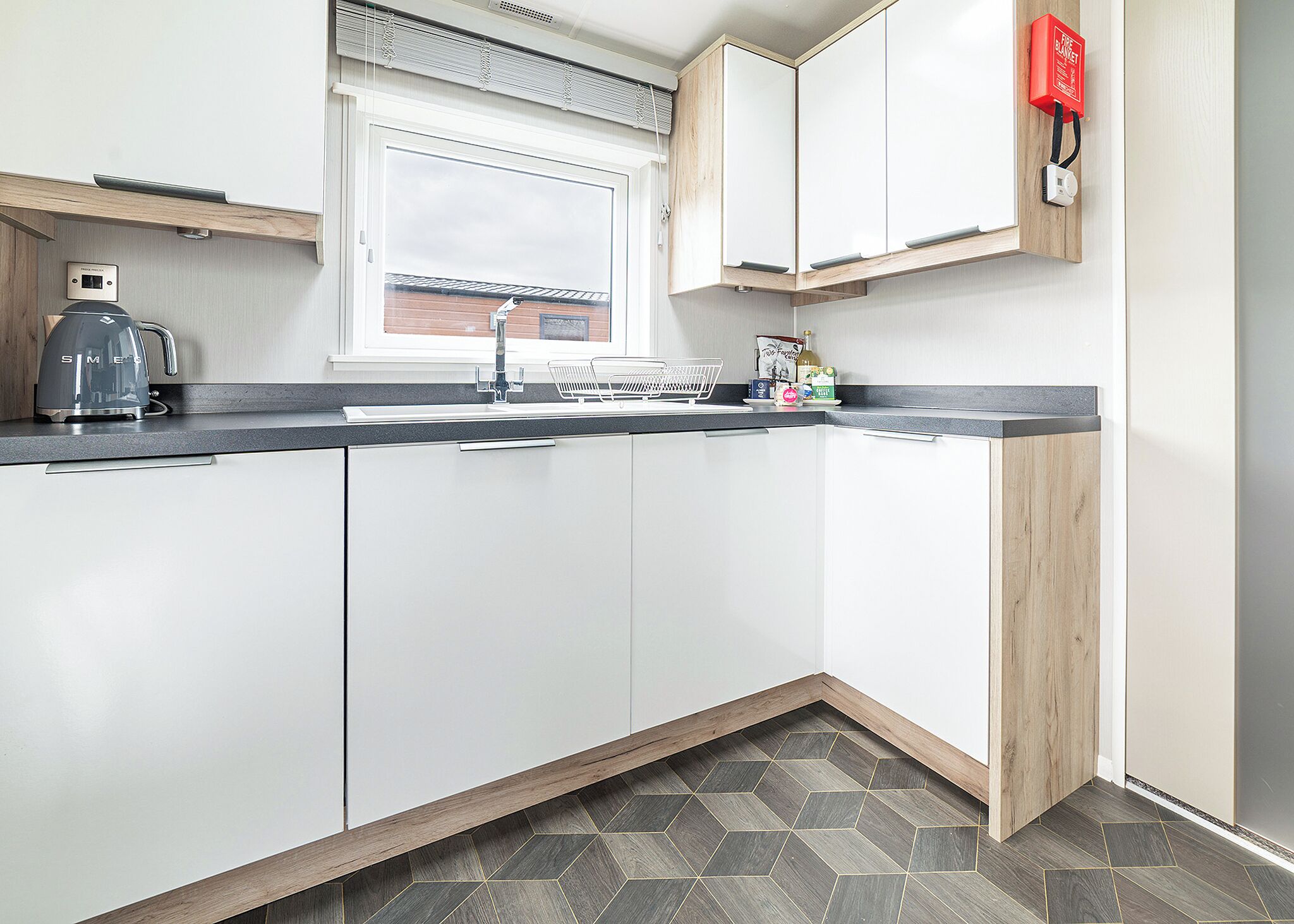 A modern kitchen with white cabinets, a black countertop, a window, and a red fire alarm.