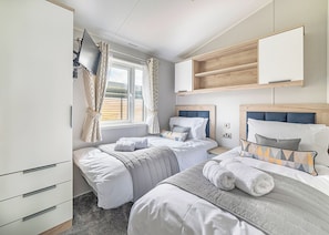 Un dormitorio con dos camas, un armario, un televisor y una ventana con cortinas.