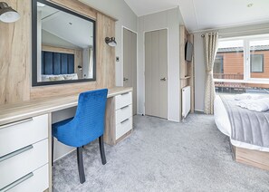 A bedroom with a bed, a desk, a chair, a mirror, and a TV.