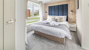 A bedroom with a bed, bedside tables, a window, and a door. - Modern two-bedroom lodge, perfect for couples or families. (Presteigne)