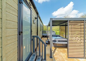 A modern building with large glass doors, a covered outdoor area with a hot tub, and a wooden deck.