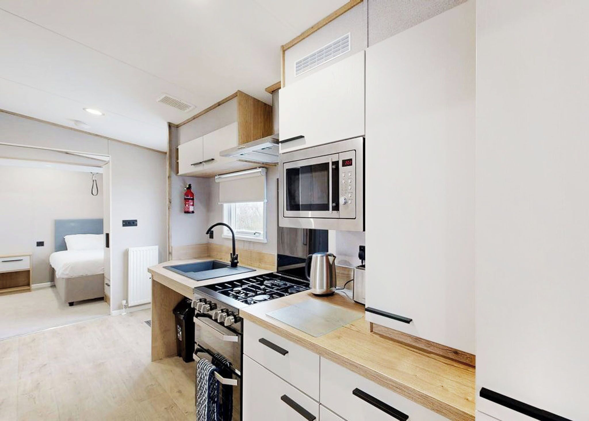 A compact kitchenette with a microwave, stove, sink, and a small window.