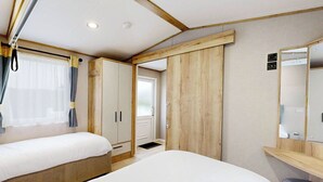 Un dormitorio con dos camas, armarios de madera, un espejo y una ventana con cortinas.