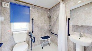 Baño con inodoro, ducha y lavamanos, todo equipado con barras de apoyo.