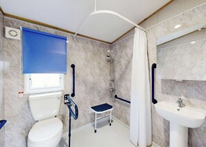 Ein Badezimmer mit Toilette, Dusche und Waschbecken, alles ausgestattet mit Haltegriffen.