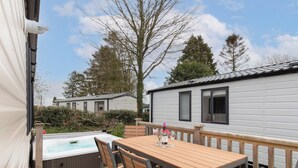 Un terrazzo in legno con vasca idromassaggio e area salotto, circondato da camper bianchi con infissi neri.