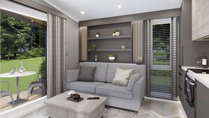 A modern living room with a grey sofa, a coffee table, and a kitchen area with a stove. - 1 bedroom accommodation in Arrochar (Arrochar)