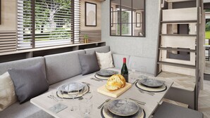 A modern dining area with a long table, grey upholstered seating, and a large window with blinds. - 1 bedroom accommodation in Arrochar (Arrochar)