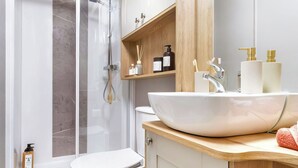 A modern bathroom with a glass shower enclosure, a white sink with gold faucets, and a toilet.