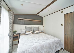 Un dormitorio con una cama grande, cabecera, mesitas de noche, una planta en maceta y una puerta de madera.