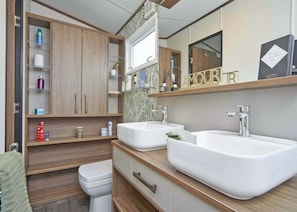 Une salle de bain moderne avec deux lavabos, des toilettes et un meuble-lavabo doté d’étagères ouvertes.