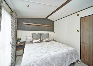 Une chambre à coucher avec un grand lit, une tête de lit, des tables de chevet, une plante en pot et une porte en bois.