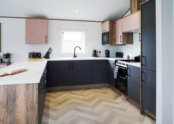 Une cuisine moderne dotée d’un îlot central, de meubles de rangement noirs, d’un four à micro-ondes, d’une machine à café et d’une cuisinière.